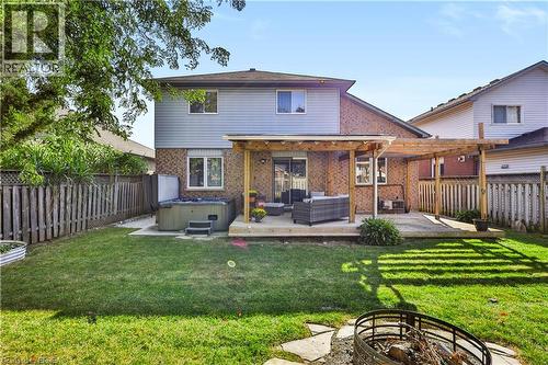 Expansive backyard featuring a green lawn, wood fence, hot tub, and a pergola-covered patio - 19 Hyslop Drive, Caledonia, ON 