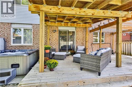 Expansive wood-finish deck with a built-in pergola, featuring a hot tub and sliding glass door entry to the home - 19 Hyslop Drive, Caledonia, ON 