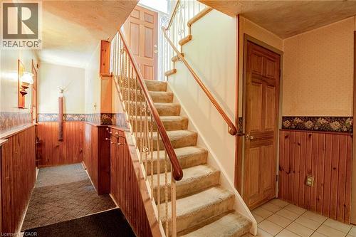 Hardwood paneling in entryway, wood-finish interior door, carpeted staircase with wood handrail, decorative metal balusters, and tiled flooring - 8 Bonnylyn Drive, Kitchener, ON 