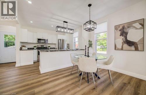 Expansive wood-finish flooring, white cabinetry, dark stone countertops, stainless steel appliances, and a glass-top dining table with a black chandelier - 185 Strange Street, Kitchener, ON - Indoor