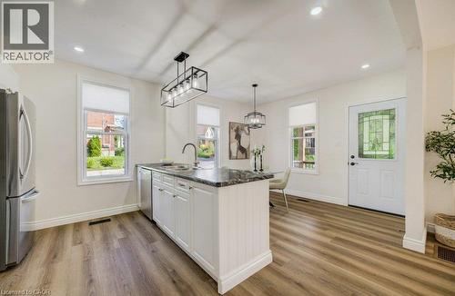 Open-concept kitchen with wood-finish flooring, white cabinetry, dark stone countertops, and stainless steel appliances - 185 Strange Street, Kitchener, ON - Indoor Photo Showing Kitchen