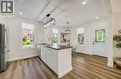 Open-concept kitchen with wood-finish flooring, white cabinetry, dark stone countertops, and stainless steel appliances - 
