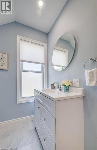 White vanity with integrated sink, polished chrome faucet, white countertop, and an oval wall mirror - 185 Strange Street, Kitchener, ON - Indoor Photo Showing Bathroom