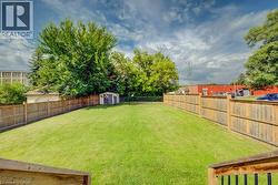 Expansive backyard featuring a manicured lawn, full privacy fencing, and a storage shed - 