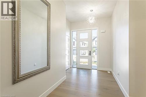 Wood-finish flooring, white walls, modern front door with frosted glass panels, full-height decorative mirror, and a contemporary ceiling light fixture - 7966 Fallon Drive Unit# 18, Lucan Biddulph (Twp), ON - Indoor Photo Showing Other Room