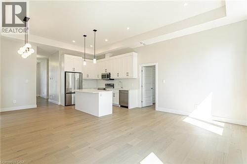 Open-concept living space with light wood-finish flooring, white kitchen cabinetry, stainless steel appliances, and a central kitchen island - 7966 Fallon Drive Unit# 18, Lucan Biddulph (Twp), ON - Indoor Photo Showing Kitchen