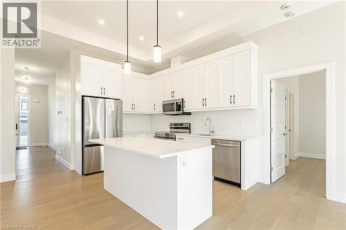 Kitchen featuring white cabinetry, stainless steel appliances, a center island with a solid surface countertop, white subway tile backsplash, and wood-finish flooring - 7966 Fallon Drive Unit# 18, Lucan Biddulph (Twp), ON - Indoor Photo Showing Kitchen With Upgraded Kitchen