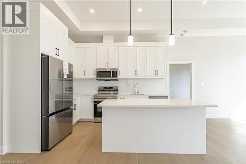Modern kitchen featuring white cabinetry, stainless steel appliances, a white tile backsplash, a central island with a light-toned countertop, and wood-finish flooring - 7966 Fallon Drive Unit# 18, Lucan Biddulph (Twp), ON - Indoor Photo Showing Kitchen With Upgraded Kitchen