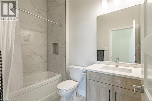 Bathtub with a tiled surround featuring a built-in niche, light-toned vanity with a white countertop and integrated sink, and an expansive wall mirror - 7966 Fallon Drive Unit# 18, Lucan Biddulph (Twp), ON - Indoor Photo Showing Bathroom