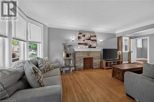 Living area featuring a stone and brick fireplace, wood-finish flooring, and multiple bay windows - 75 Barons Avenue S, Hamilton, ON 