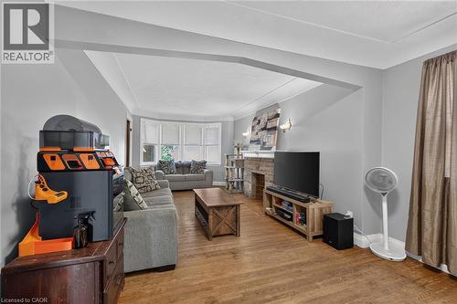 Hardwood flooring extending throughout, bay window with multiple panes, stone-clad fireplace with mantel, recessed ceiling details, and neutral wall tones - 75 Barons Avenue S, Hamilton, ON 