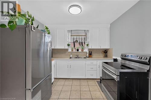 Kitchen featuring white cabinetry, stainless steel appliances, tiled backsplash, and neutral tile flooring - 75 Barons Avenue S, Hamilton, ON 