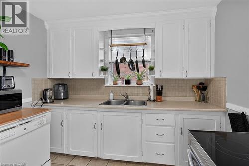 White cabinetry, light-toned countertops, tiled backsplash, stainless steel double sink, and integrated dishwasher - 75 Barons Avenue S, Hamilton, ON 