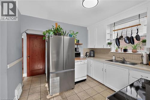 Kitchen featuring white cabinetry, a double basin stainless steel sink, tiled backsplash, and light-colored countertops - 75 Barons Avenue S, Hamilton, ON 