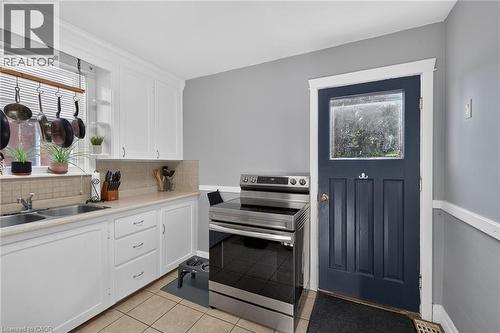 White cabinetry, stainless steel range, tile flooring, window with natural light, and a paneled door with glass insert - 75 Barons Avenue S, Hamilton, ON 