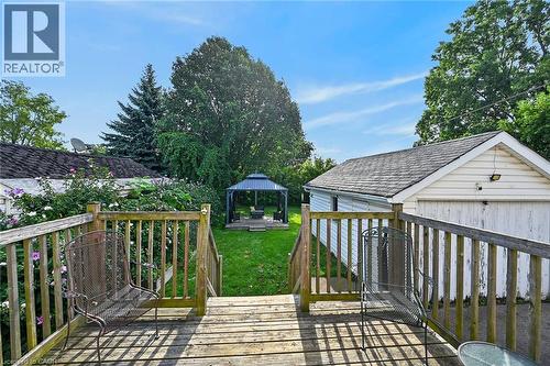 Expansive backyard featuring a wood deck, a manicured lawn, mature trees, and a detached garage with siding - 75 Barons Avenue S, Hamilton, ON 