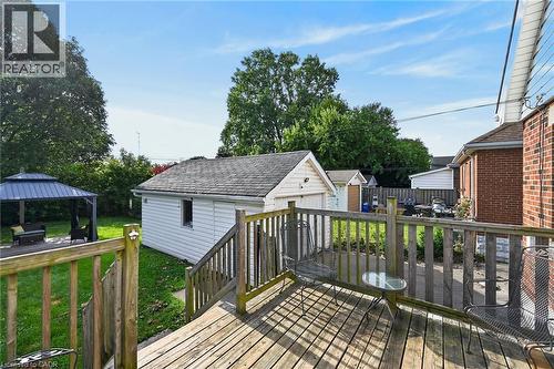 Expansive wood deck with railings, leading to a landscaped backyard featuring a detached garage and a paved patio with a gazebo - 75 Barons Avenue S, Hamilton, ON 