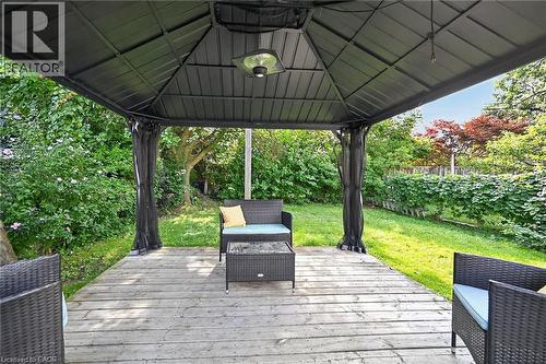 Expansive outdoor gazebo featuring a wood deck surface, black metal frame, and an integrated ceiling light fixture, surrounded by mature landscaping - 75 Barons Avenue S, Hamilton, ON 