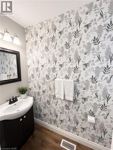 Wood-finish flooring, half-pedestal vanity with integrated sink, black framed mirror, and botanical print wallpaper - 765 Angler Way, Waterloo, ON - Indoor Photo Showing Bathroom