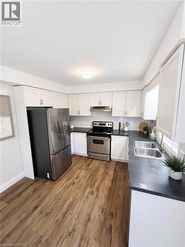 Wood-finish flooring, white cabinetry, dark countertops, stainless steel appliances, and a double basin sink - 765 Angler Way, Waterloo, ON - Indoor Photo Showing Kitchen With Double Sink