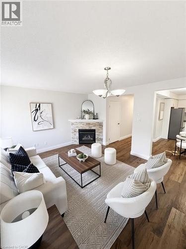 Living area featuring wood-finish flooring, a stone-clad fireplace, and a contemporary chandelier - 765 Angler Way, Waterloo, ON - Indoor Photo Showing Living Room With Fireplace
