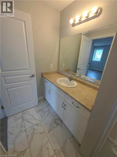 White flat-panel cabinetry, a light-toned countertop, an integrated sink, a rectangular mirror, and a four-bulb vanity light fixture - 998 Mapleridge Street, London, ON - Indoor Photo Showing Bathroom