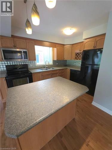 Kitchen featuring wood cabinetry, stainless steel microwave, black appliances, and a central island with a solid surface countertop - 998 Mapleridge Street, London, ON - Indoor Photo Showing Kitchen With Double Sink