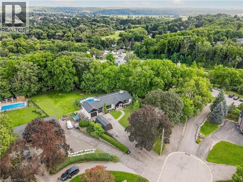 Lush, mature landscaping surrounds the property, featuring a private swimming pool, extensive paved driveways, and a single-story residence with a dark roof - 267 Abraham Street, Cambridge, ON - Outdoor With View