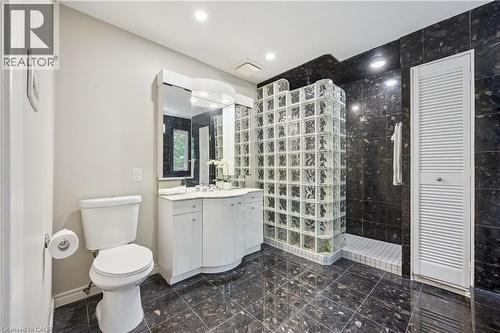 Tiled flooring, white vanity with integrated sink, glass block shower enclosure, dark tiled shower surround, recessed lighting - 267 Abraham Street, Cambridge, ON - Indoor Photo Showing Bathroom