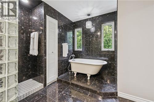 Freestanding clawfoot bathtub, two windows, glass block shower enclosure, dark large format tile flooring, and dark large format tile wall surround - 267 Abraham Street, Cambridge, ON - Indoor Photo Showing Bathroom