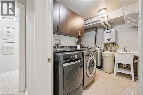 Utility room featuring dark wood-finish cabinetry, a black patterned countertop, a utility sink, and a wall-mounted water heater - 267 Abraham Street, Cambridge, ON - Indoor Photo Showing Laundry Room