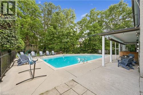 Outdoor swimming pool with a surrounding concrete patio, covered patio area, and mature trees providing natural screening - 267 Abraham Street, Cambridge, ON - Outdoor With In Ground Pool