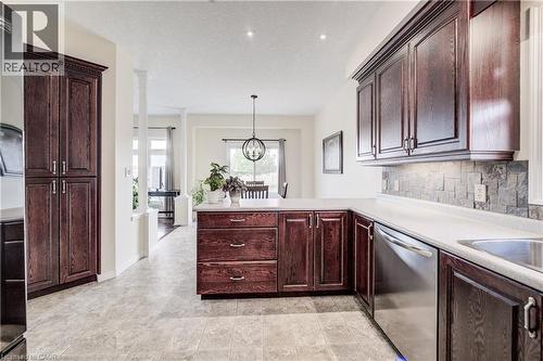 Kitchen featuring dark wood-finish cabinetry, light-toned countertops, slate look backsplash, stainless steel dishwasher, - 64 Kropf Drive, Baden, ON - Indoor Photo Showing Kitchen