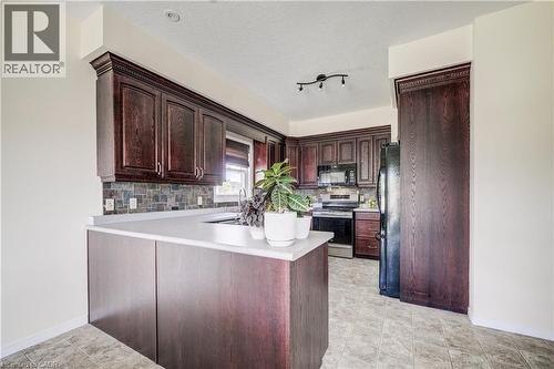 Kitchen featuring dark wood-finish cabinetry, light-toned countertops, and a slate backsplash - 64 Kropf Drive, Baden, ON - Indoor Photo Showing Kitchen