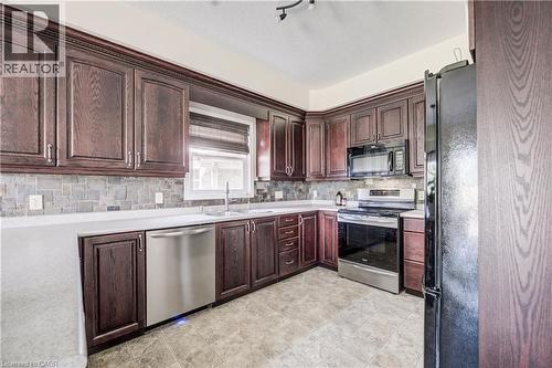 Dark wood-finish cabinetry with crown molding, stainless steel appliances, light-toned countertops, and a slate backsplash - 64 Kropf Drive, Baden, ON - Indoor Photo Showing Kitchen