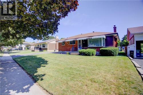 Brick exterior with a prominent chimney, front yard with manicured landscaping, covered front porch, and an attached carport - 52 Queenston Crescent, Kitchener, ON - Outdoor