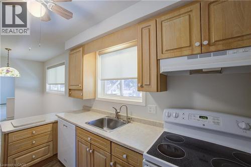 Kitchen featuring light wood-finish cabinetry, light-toned countertops, a stainless steel sink with a chrome faucet, and white appliances including a range and dishwasher - 52 Queenston Crescent, Kitchener, ON - Indoor Photo Showing Kitchen