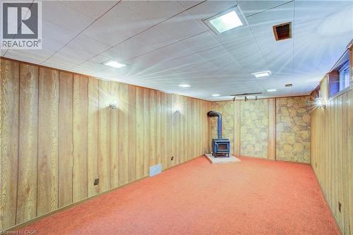 Finished basement space featuring wood paneling, a stone accent wall, recessed lighting, and a wood-burning stove with a stone hearth - 52 Queenston Crescent, Kitchener, ON - Indoor