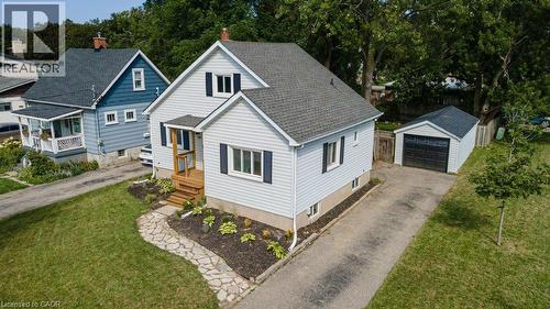 Light-colored siding exterior with dark shutters, covered porch with natural wood railing, stone-finish walkway, detached garage with black garage door, and a paved driveway - 99 Shantz Lane, Kitchener, ON - Outdoor