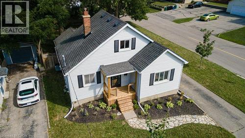 Light-colored siding exterior with dark shutters, covered porch with natural wood railing, dark shingle roof, and brick chimney - 99 Shantz Lane, Kitchener, ON - Outdoor