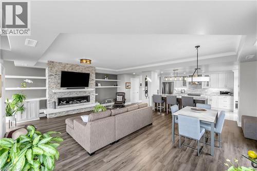 Open-concept living space featuring wood-finish flooring, a stone-clad fireplace with a mantle, built-in shelving, and a kitchen with white cabinetry and stainless steel appliances - 1477 Lakeshore Road Unit# Ph 1, Burlington, ON 