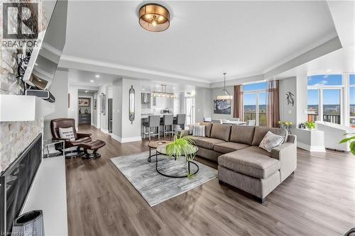 Open-concept living area featuring wood-finish flooring, a stone-accented fireplace, recessed lighting, and large windows with elevated outdoor scenery - 1477 Lakeshore Road Unit# Ph 1, Burlington, ON 