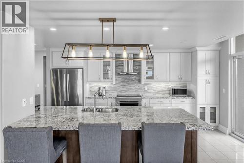 Kitchen featuring an island with stone countertops, a stainless steel sink with a gooseneck faucet, white cabinetry, and stainless steel appliances - 1477 Lakeshore Road Unit# Ph 1, Burlington, ON 