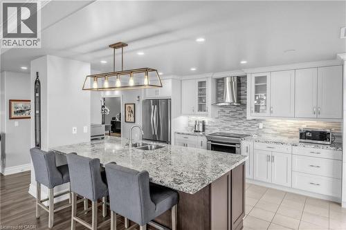 Kitchen featuring a large island with an undermount sink, pendant lighting, stainless steel appliances, white cabinetry, and a tile backsplash - 1477 Lakeshore Road Unit# Ph 1, Burlington, ON 