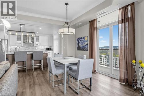 Open-concept living space featuring wood-finish flooring, a kitchen island with seating, white cabinetry, and a full-height tile backsplash - 1477 Lakeshore Road Unit# Ph 1, Burlington, ON 