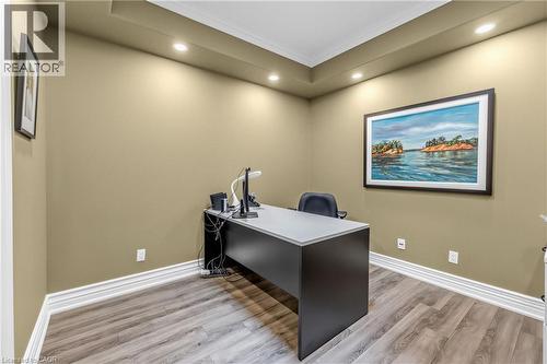 Professional home office featuring a sleek dark desk with white work surface, ergonomic task seating, warm neutral wall finishes, recessed ceiling lighting, wood-finish flooring, and framed landscape - 1477 Lakeshore Road Unit# Ph 1, Burlington, ON 