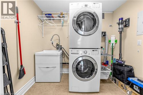 Laundry area featuring a stacked washer and dryer, utility sink with a gooseneck faucet, and wall-mounted shelving - 1477 Lakeshore Road Unit# Ph 1, Burlington, ON 