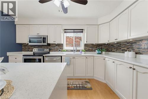 White cabinetry, stainless steel appliances, mosaic tile backsplash, solid surface countertops, and wood-finish flooring - 592 Little Dover Crescent, Waterloo, ON - Indoor Photo Showing Kitchen