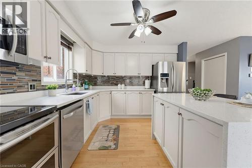 White cabinetry with dark hardware, stone-finish countertops, stainless steel appliances, wood-finish flooring, and a multi-tone tile backsplash - 592 Little Dover Crescent, Waterloo, ON - Indoor Photo Showing Kitchen With Upgraded Kitchen
