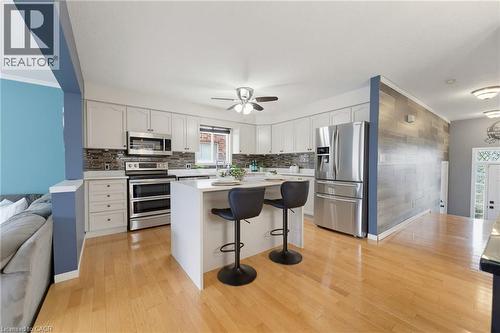 Kitchen featuring wood-finish flooring, white cabinetry, a large kitchen island, stainless steel appliances, and a tiled backsplash - 592 Little Dover Crescent, Waterloo, ON - Indoor Photo Showing Kitchen With Upgraded Kitchen